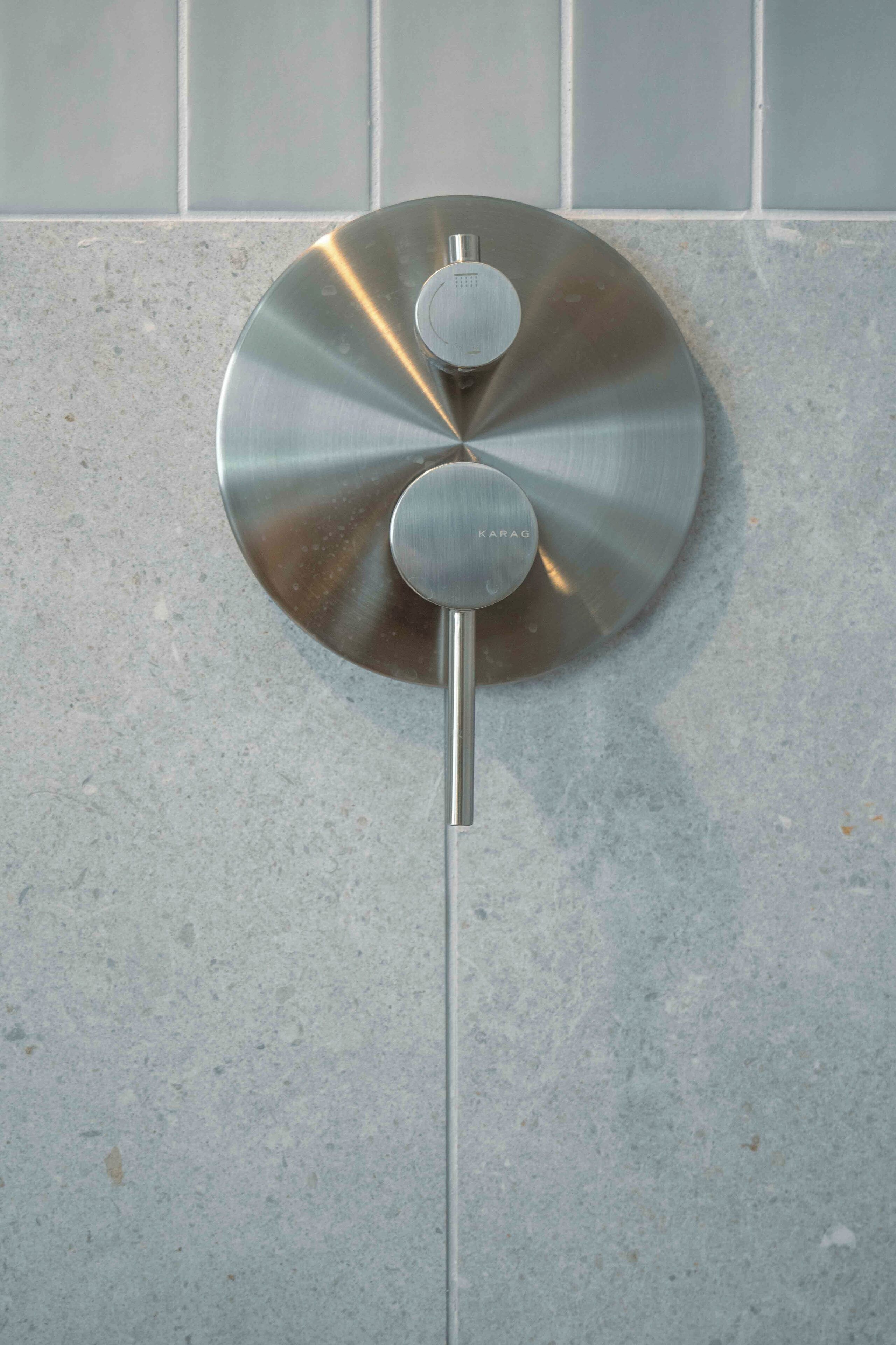 A metallic, circular object with a central knob and a long rod, mounted on a tiled wall.