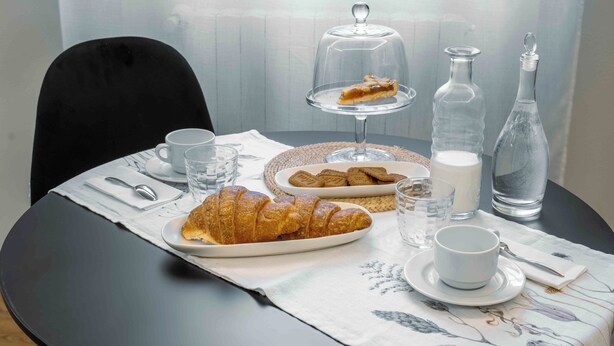 A dining table with croissants, a glass of water, a cup, a bottle, and a glass of milk. - La Croce Apartments (Castelnovo ne' Monti)