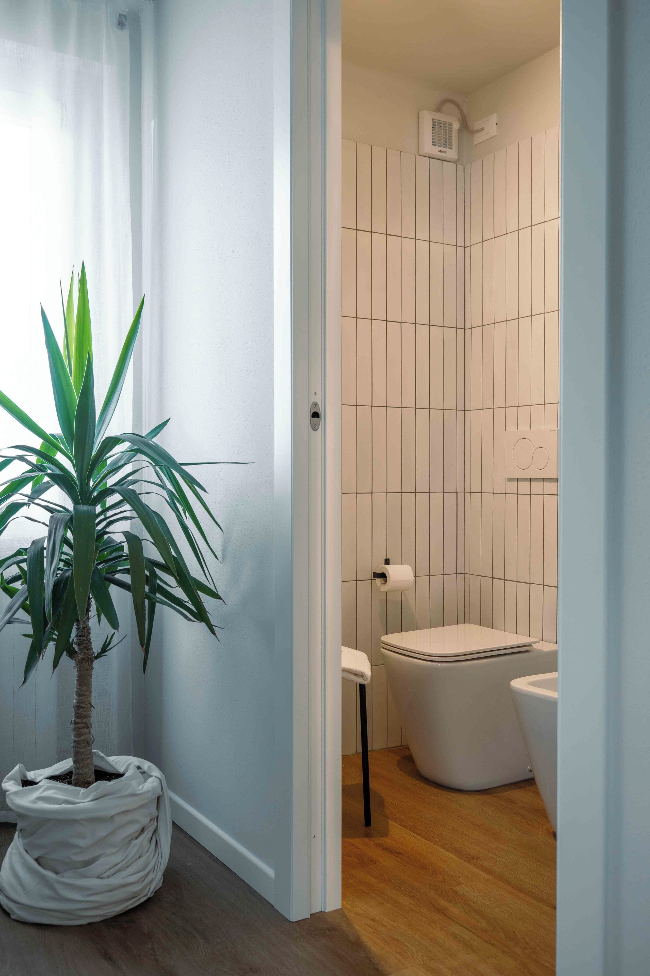 A bathroom with a toilet, bidet, and a shower area. There is a potted plant in the corner.