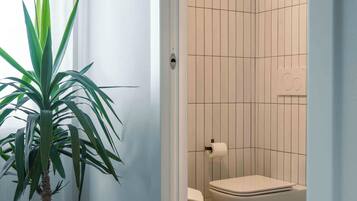 A bathroom with a toilet, bidet, and a shower area. There is a potted plant in the corner.