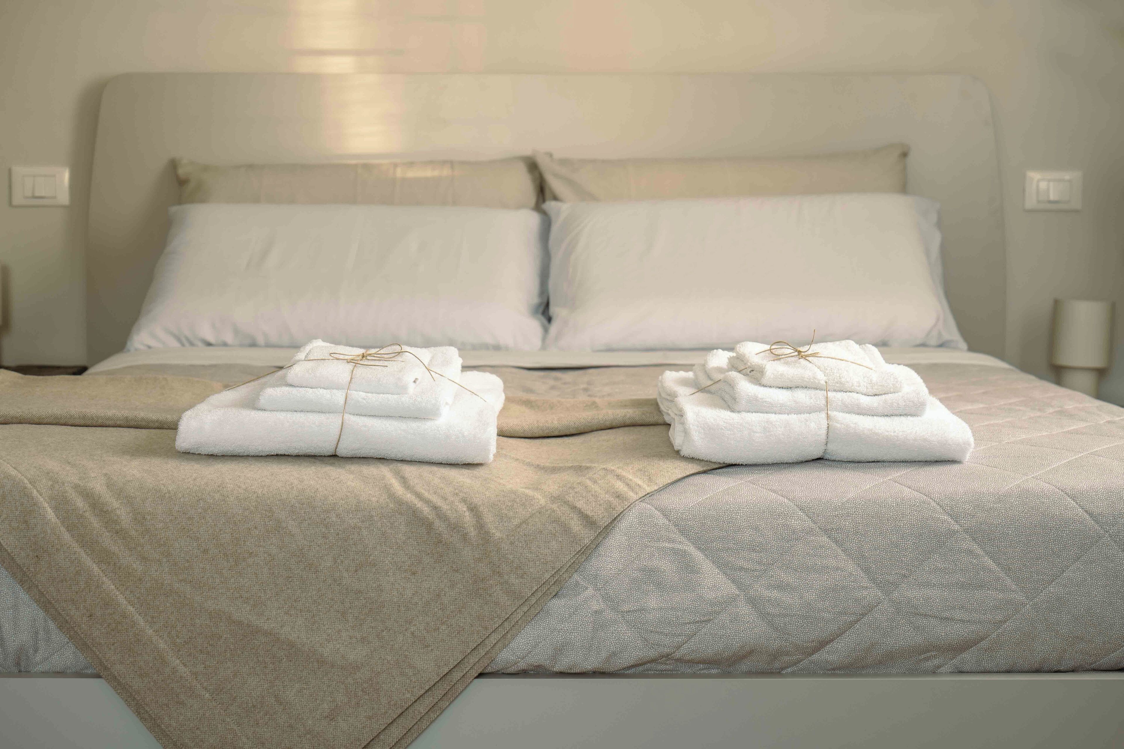 Ein ordentlich gemachtes Bett mit zwei gefalteten weißen Handtüchern und einer beigen Tagesdecke.