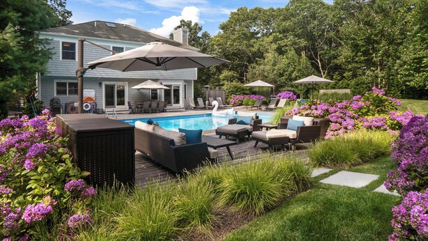 A backyard with a swimming pool, outdoor furniture, and a house. - Southampton 4BR Home | Heated Pool, Firepit, Large Backyard (Hamptons)