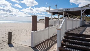 A wooden boardwalk leading to a beach area with a sign reading "COOPER'S BEACH" established in 1934. - Southampton 4BR Home | Heated Pool, Firepit, Large Backyard (Hamptons)