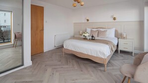 A bedroom with a bed, bedside tables, a radiator, a wooden ceiling decoration, and a view through a glass door.