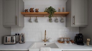 A kitchen with a white sink, two toasters, a coffee maker, and a shelf with cups and a plant.