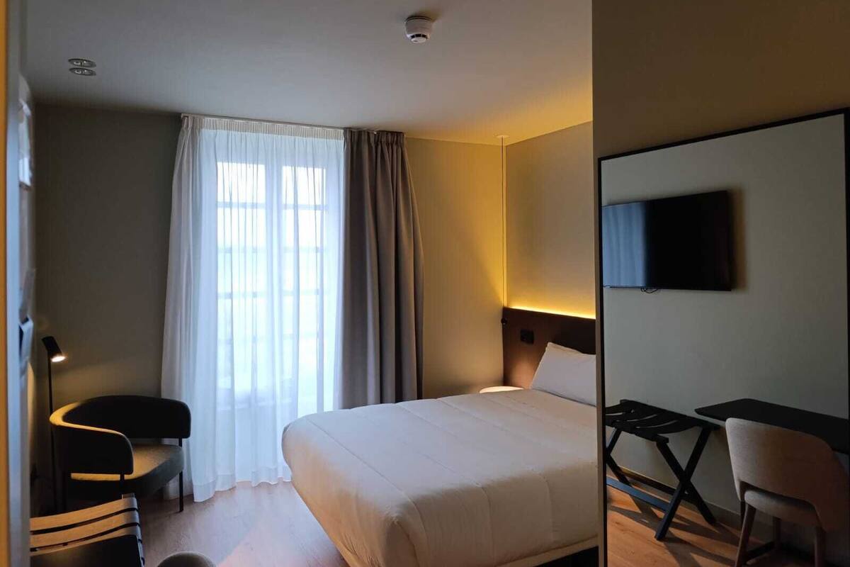 A hotel room with a bed, a desk, a chair, and a TV.