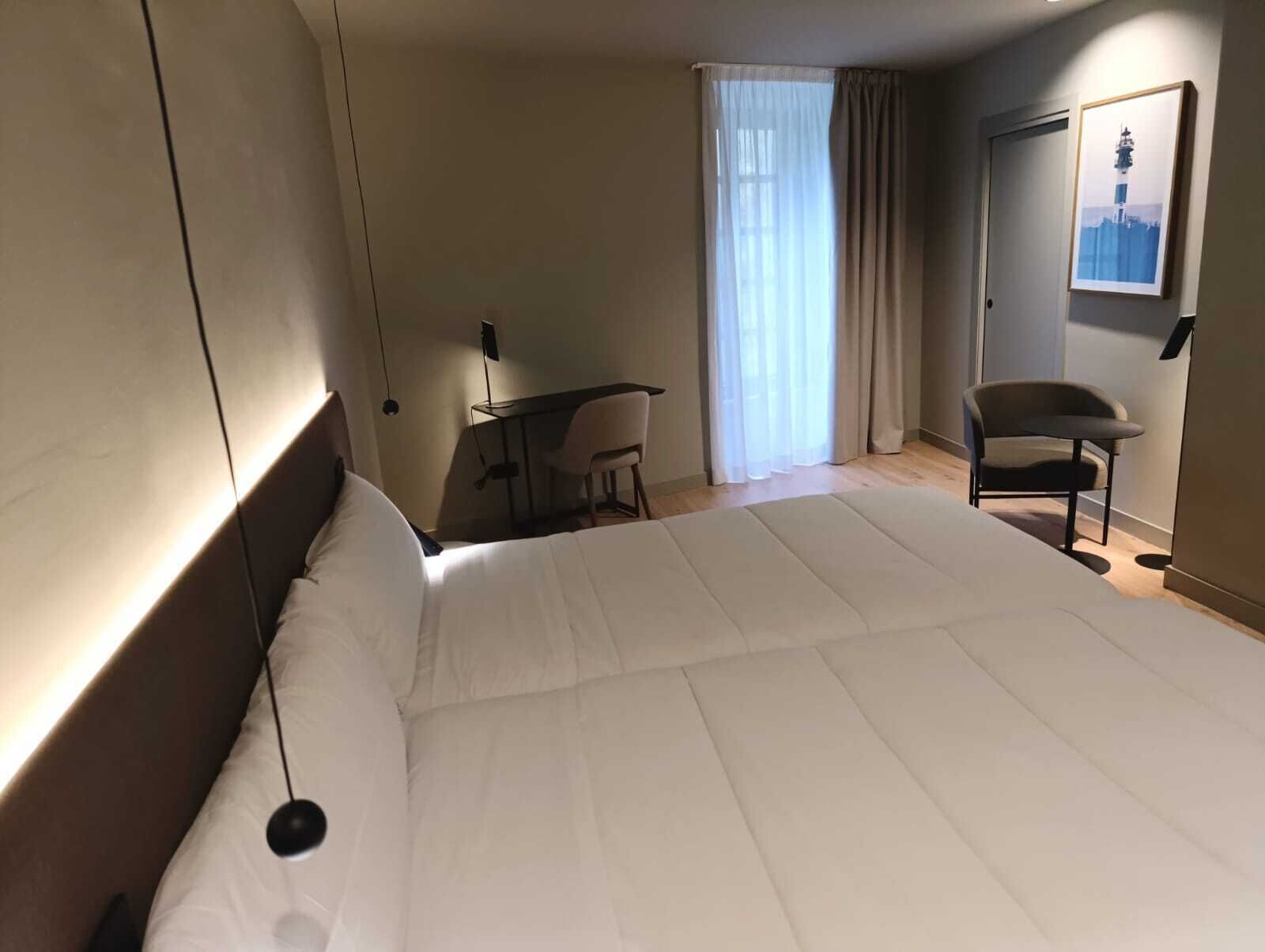 A hotel room with a large bed, a desk, a chair, and a window with curtains.