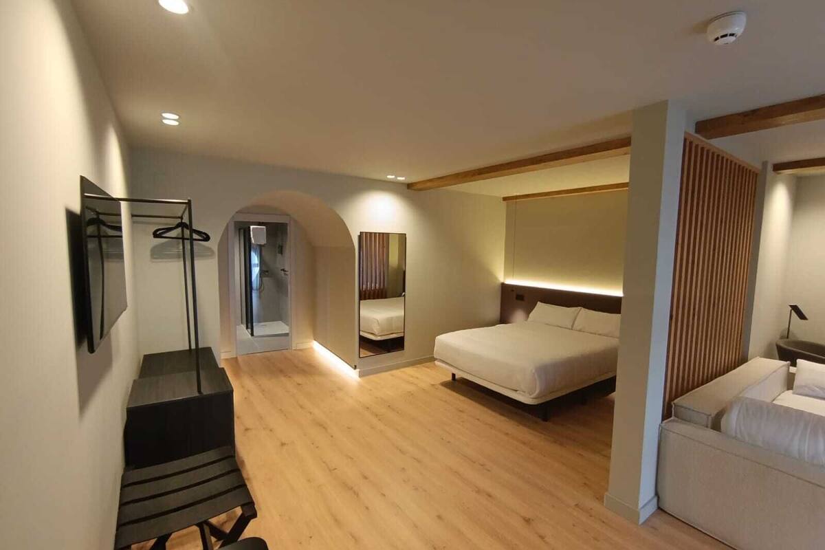 A modern hotel room with a wooden floor, a bed, a desk, and a walk-in closet.