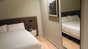 Un dormitorio con cama, mesita de noche con teléfono, espejo en la pared y un cuadro enmarcado.