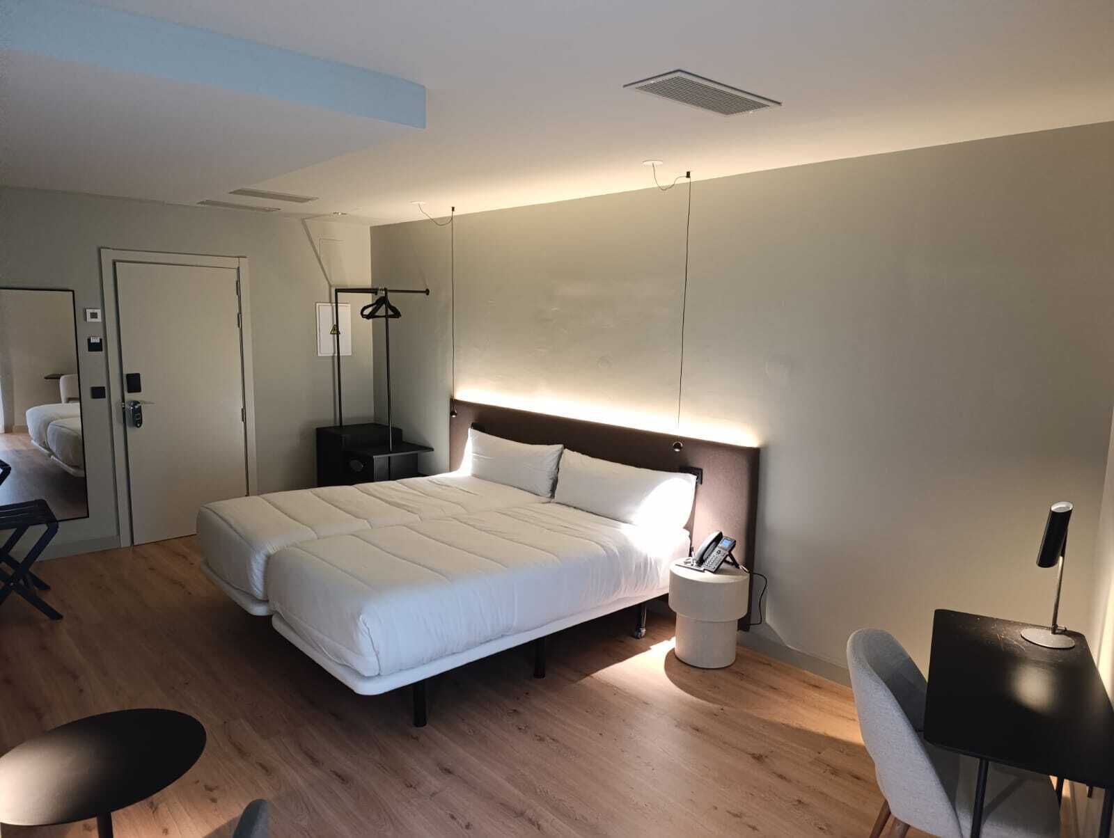 A modern hotel room with a large bed, bedside tables, a desk, and a chair.