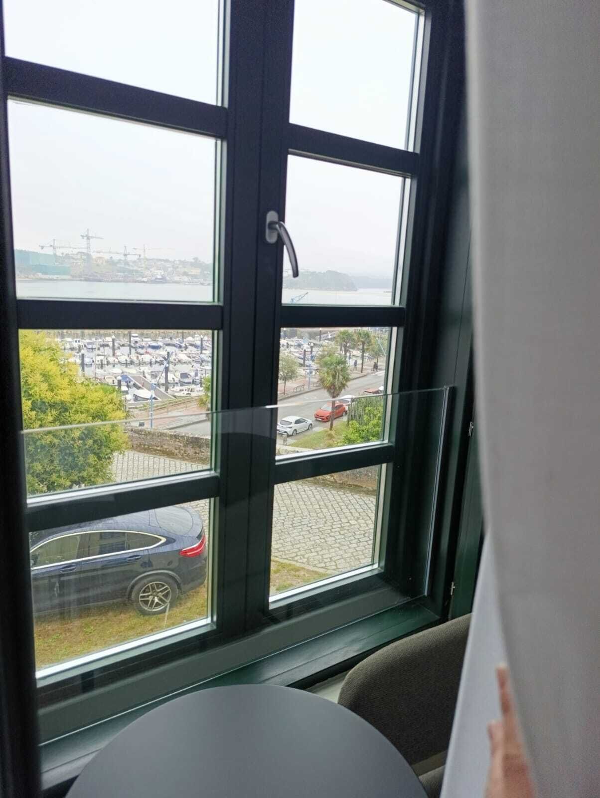 Una habitación con un ventanal que ofrece vistas a un estacionamiento y un cuerpo de agua distante.
