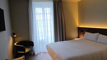 Habitación de hotel con una cama grande, una silla, un escritorio y un ventanal con cortinas.