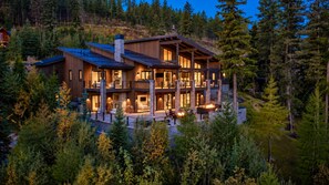 Une maison en bois à plusieurs étages, dotée d’un balcon et entourée d’une forêt dense.