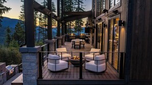An outdoor deck with a fire pit, seating, and a view of the mountains. - Breathtaking ski residence - theater room , sauna , gym, heated driveway and hot tub deck (Whitefish)