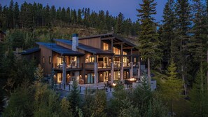 Un chalet à plusieurs étages doté d’une cheminée en pierre, d’un espace extérieur aménagé et offrant une vue sur la forêt environnante.
