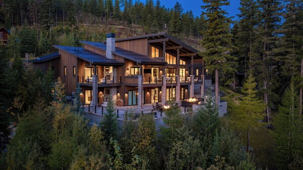 A multi-story wooden cabin with a stone chimney, surrounded by dense forest.