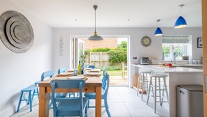 Une cuisine moderne avec une table en bois et des chaises bleues, une grande fenêtre et une vue sur le jardin.