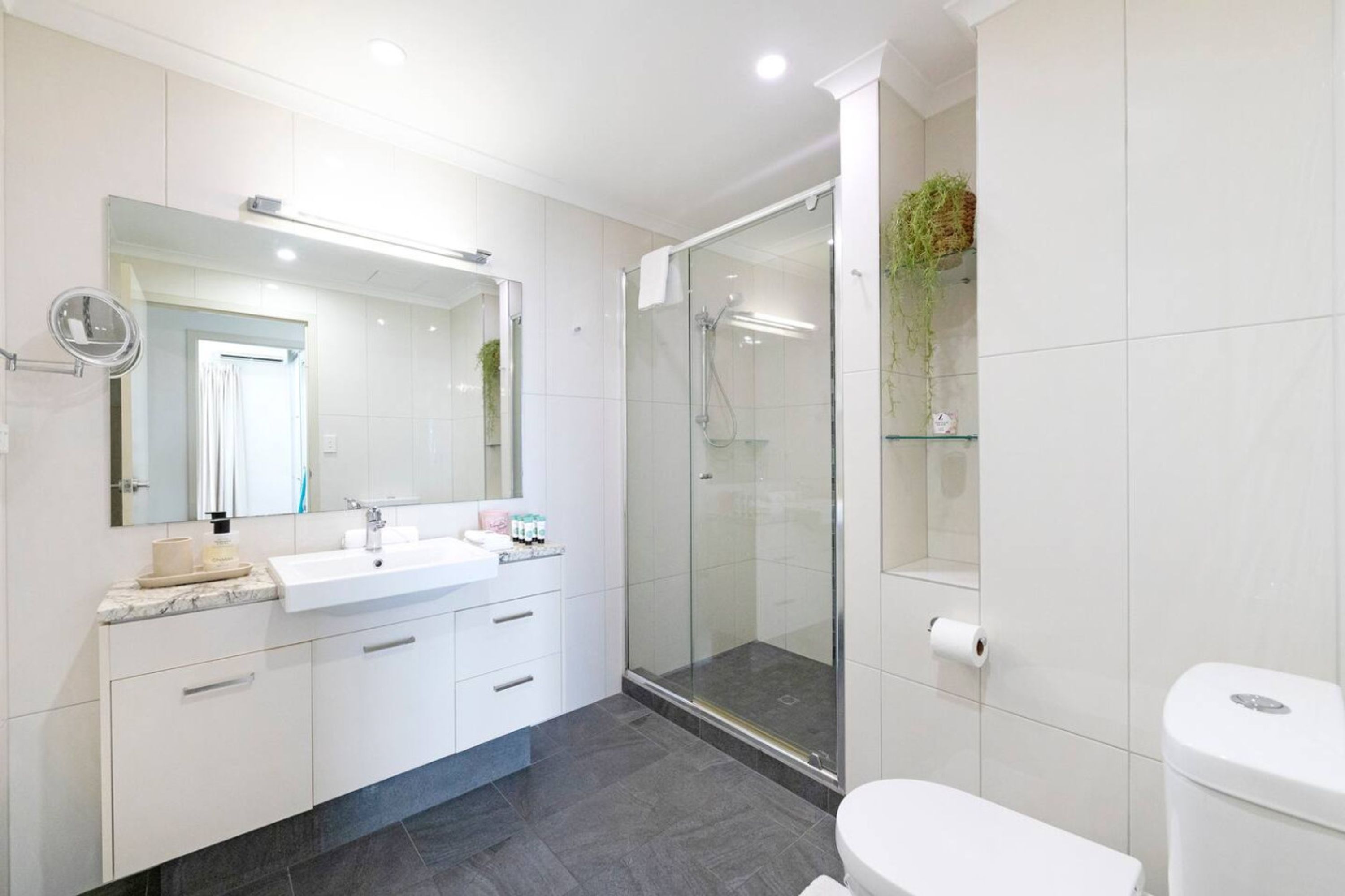 Un baño moderno con ducha envuelta en vidrio, un lavabo blanco con encimera de mármol y un espejo grande sobre el lavabo.