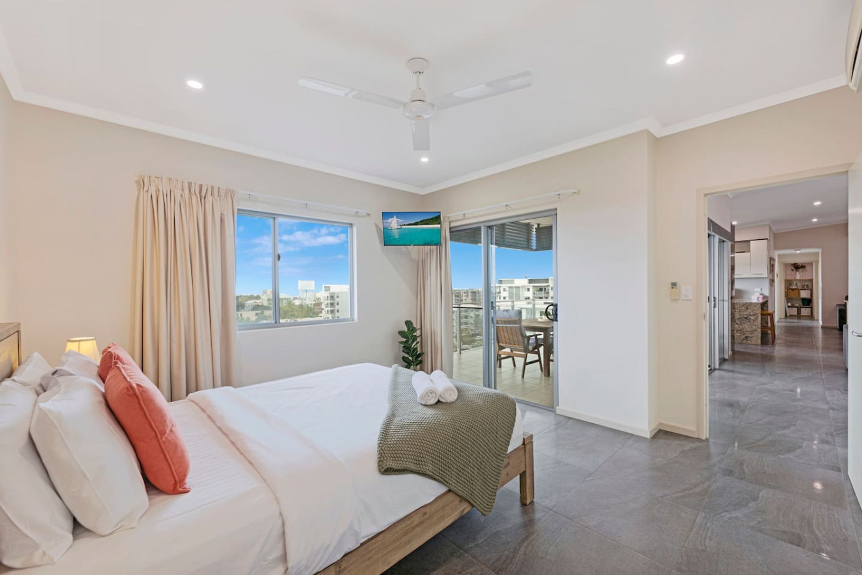Una habitación de hotel moderna con una cama grande, un ventilador de techo y un balcón con vista a la ciudad.