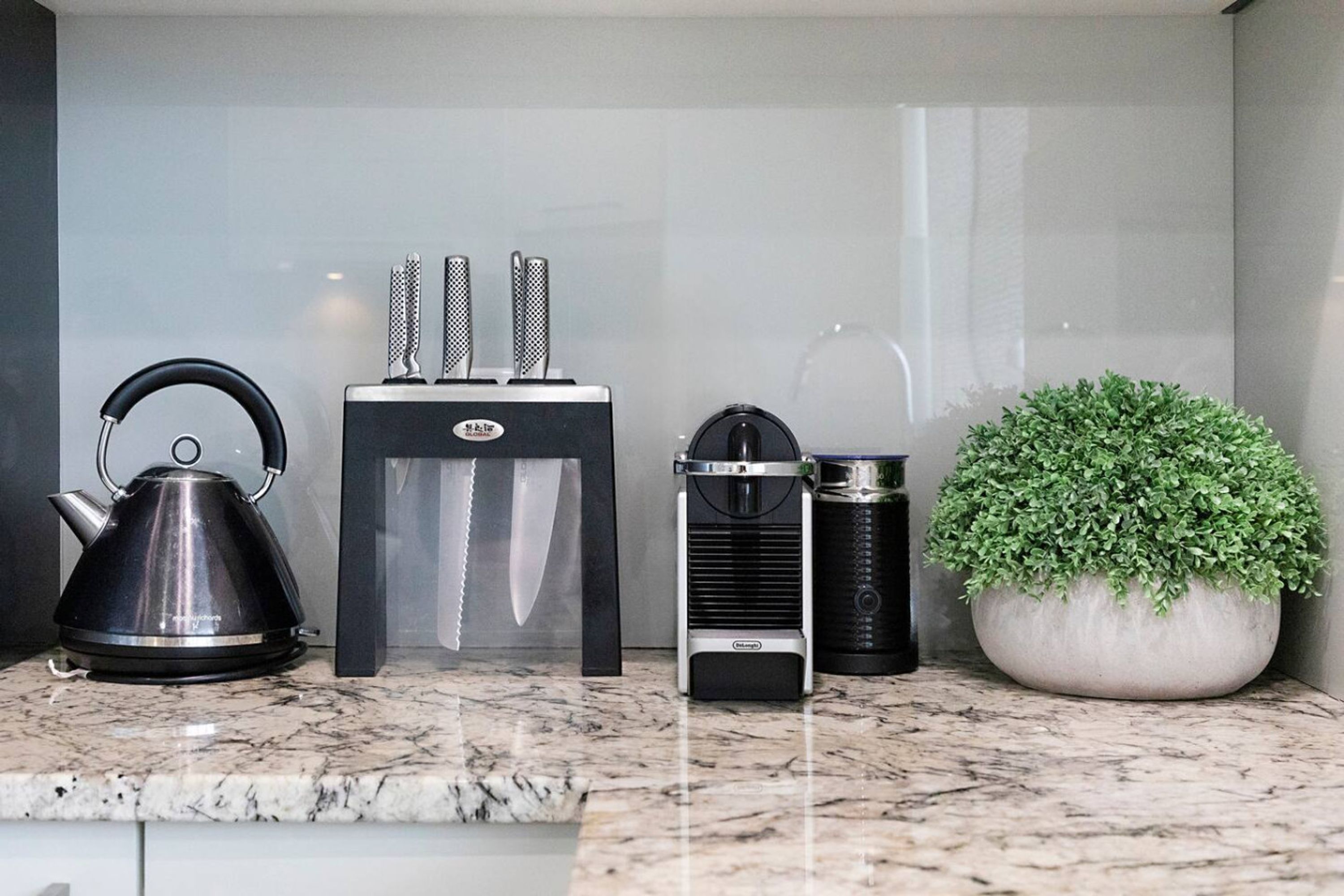 A kitchen counter with a kettle, a coffee maker, a knife block, and a potted plant.