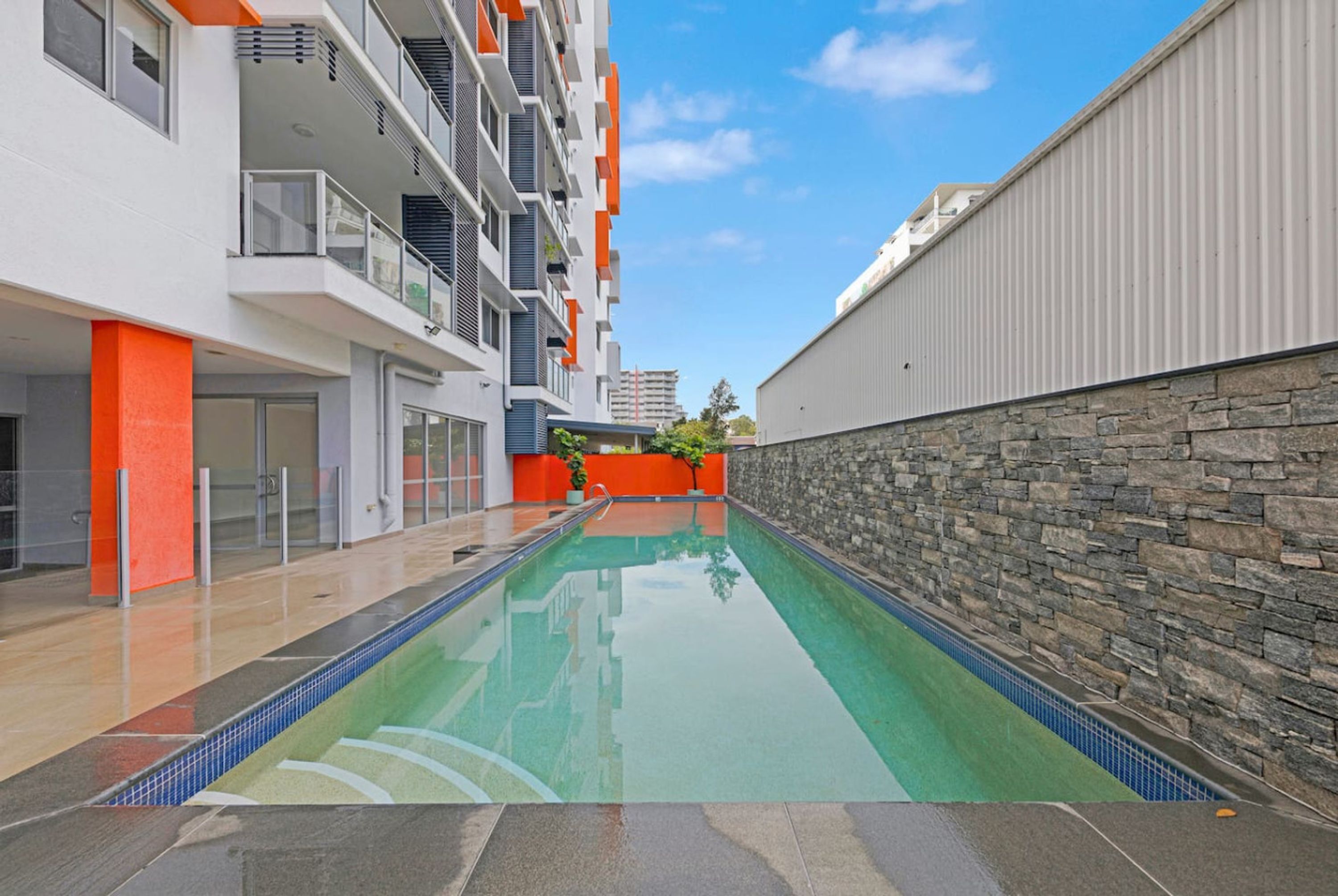 A modern building with a swimming pool, stone wall, and orange accents.
