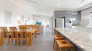 A modern kitchen with a marble countertop, wooden chairs, and ceiling fans. - Zen Coastline Pool - Balcony Dining - Seaview (Darwin)