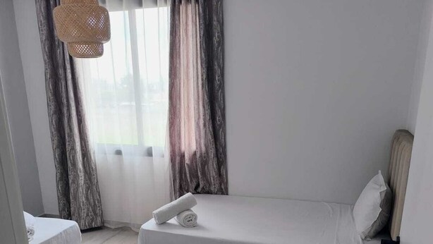 Een moderne slaapkamer met een enkel bed, een nachtkastje, een hanglamp en uitzicht door een raam met gordijnen.