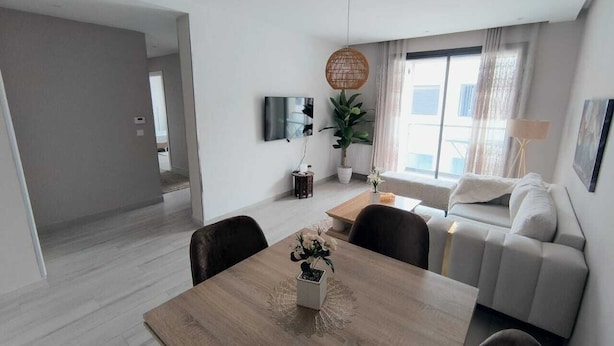 A modern living room with a dining table, sofa, and a large window. - Charmant Appart Punique au Cœur de Carthage (Carthage)