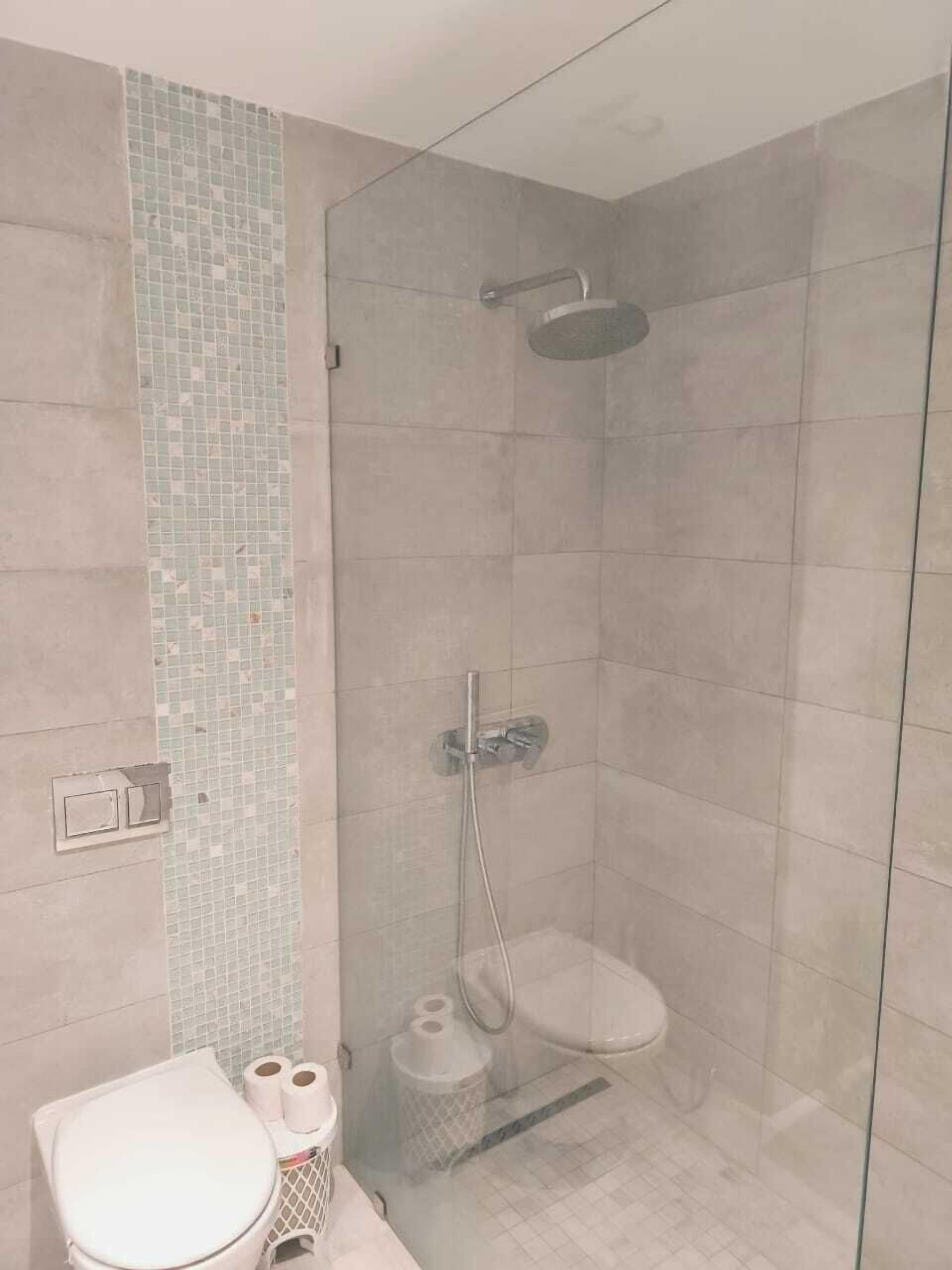 A modern bathroom with a glass-enclosed shower, a toilet, and a small trash bin.