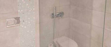 A modern bathroom with a glass-enclosed shower, a toilet, and a small trash bin.