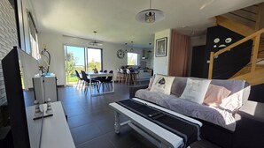 A modern living room with a sofa, a dining table, and a kitchen in the background.