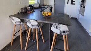 A modern kitchen with a central island, bar stools, a large wall clock, pendant lights, and a 'HOME' sign.