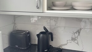 Una cocina con protector contra salpicaduras de mármol, encimera negra, tostadora, tetera y un mueble con tirador plateado.