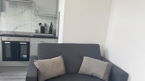 Una sala de estar moderna con un sofá gris, una zona de cocina con baldosas de mármol y un piso gris.