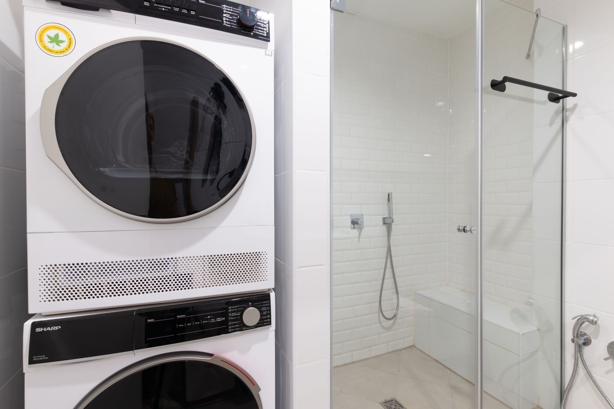 A front-loading washing machine and a glass-enclosed shower area with a handheld showerhead.