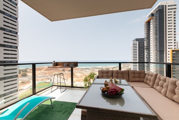 Un balcón moderno con una mesa de vidrio, sofá color beige y vistas a la ciudad y la costa.