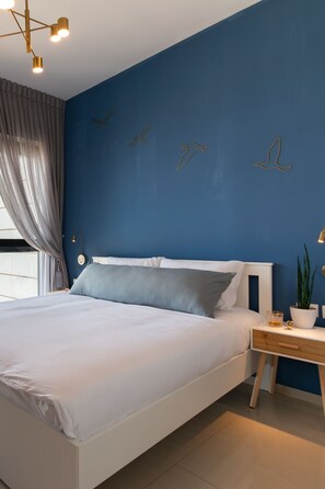 Un dormitorio moderno con una pared azul como detalle, una cama blanca y decoración en la pared.