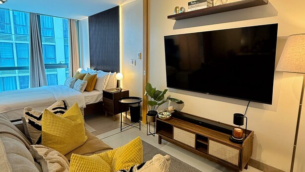 Et moderne hotelværelse med en stor seng, en sofa, et fjernsyn og en balkon med gardiner.