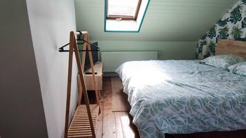 Ein Schlafzimmer mit schrägen Wänden, einem Bettgestell aus Holz, einem Heizkörper und einem Fenster mit Blick auf den Himmel.