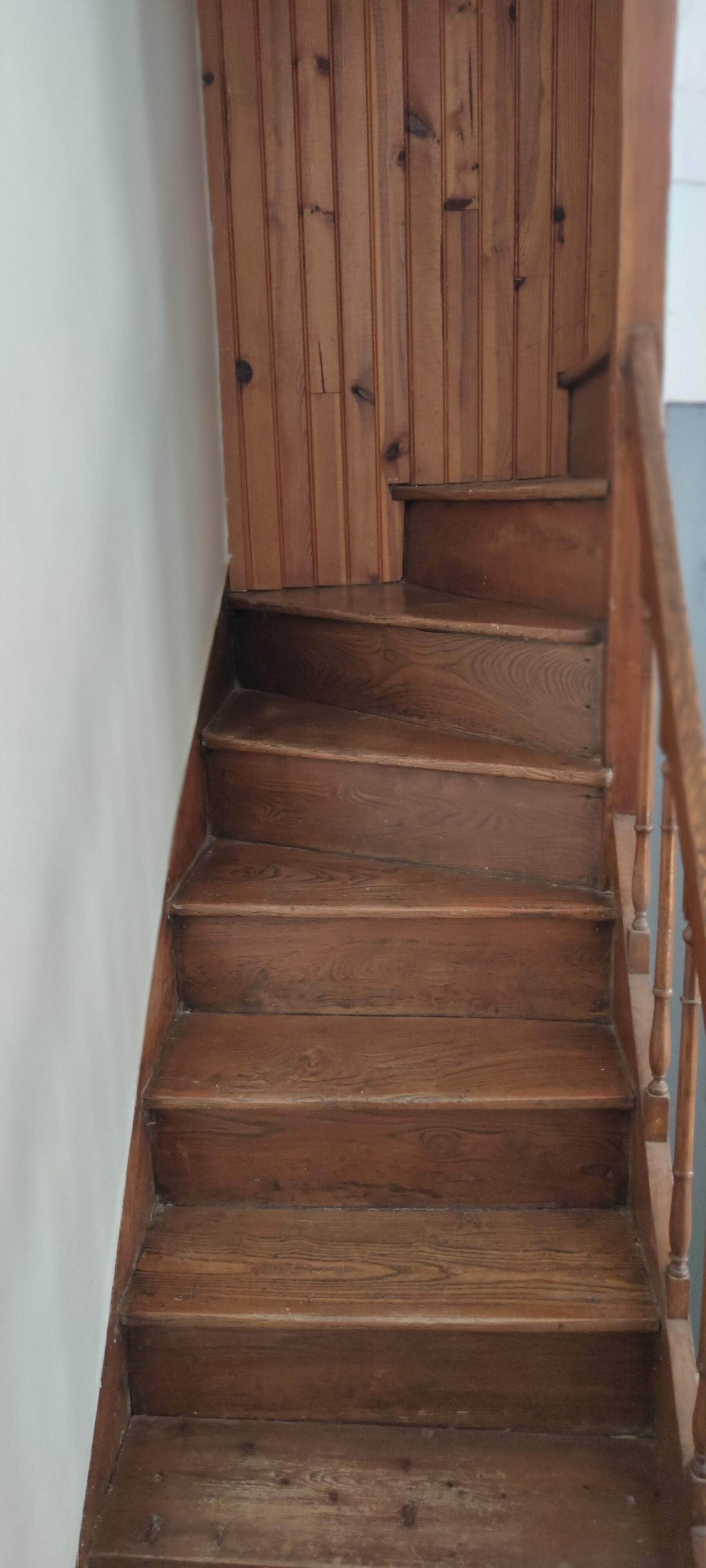 Un escalier en bois, doté d’une rampe et bordé d’un mur blanc d’un côté.