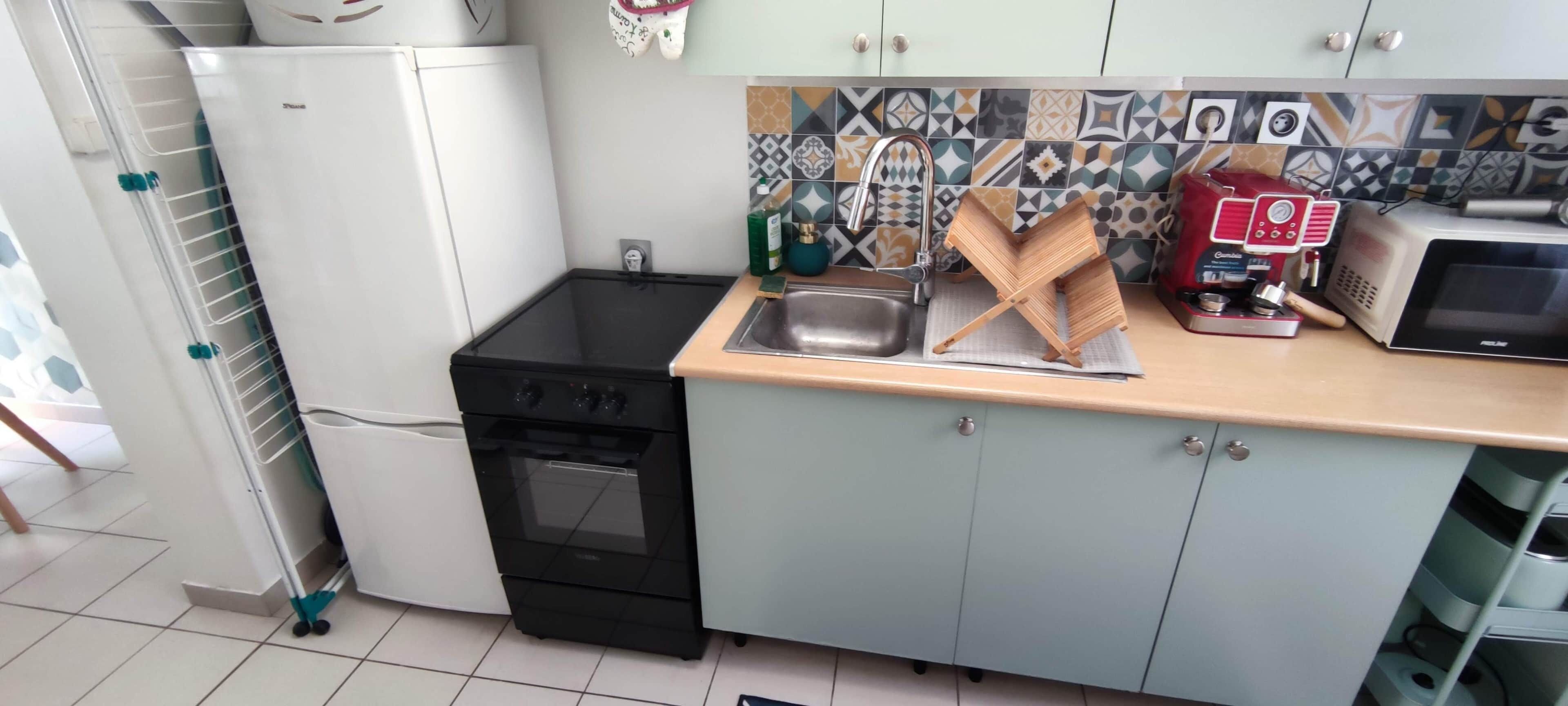 Eine kleine Küche mit einem schwarzen Ofen, einer Mikrowelle, einer Kaffeemaschine und einem Spülbecken.