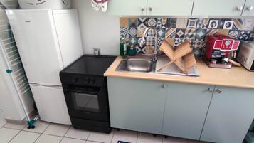 Eine kleine Küche mit einem schwarzen Ofen, einer Mikrowelle, einer Kaffeemaschine und einem Spülbecken.