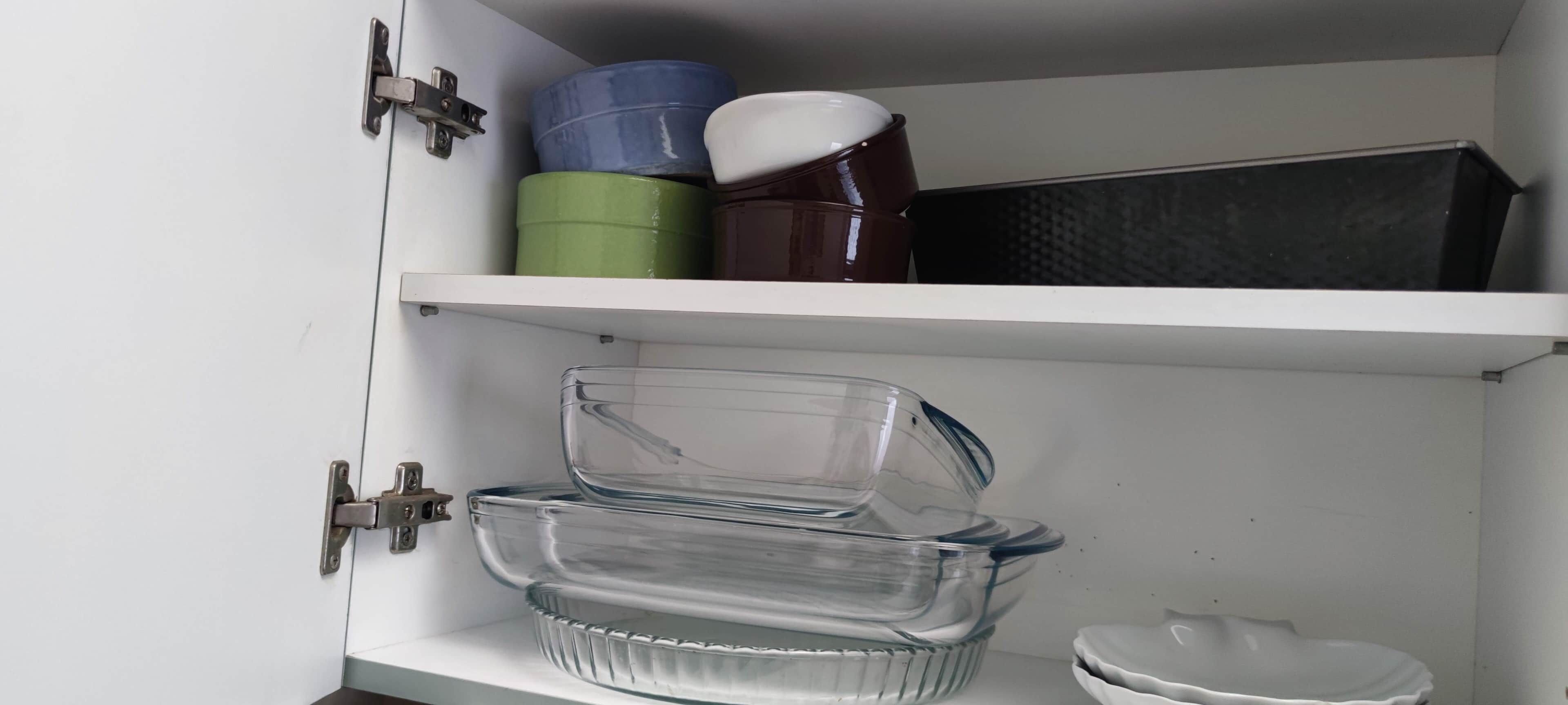 Un meuble de cuisine avec un égouttoir à vaisselle en verre, une assiette blanche et un appareil noir posé sur l’étagère.