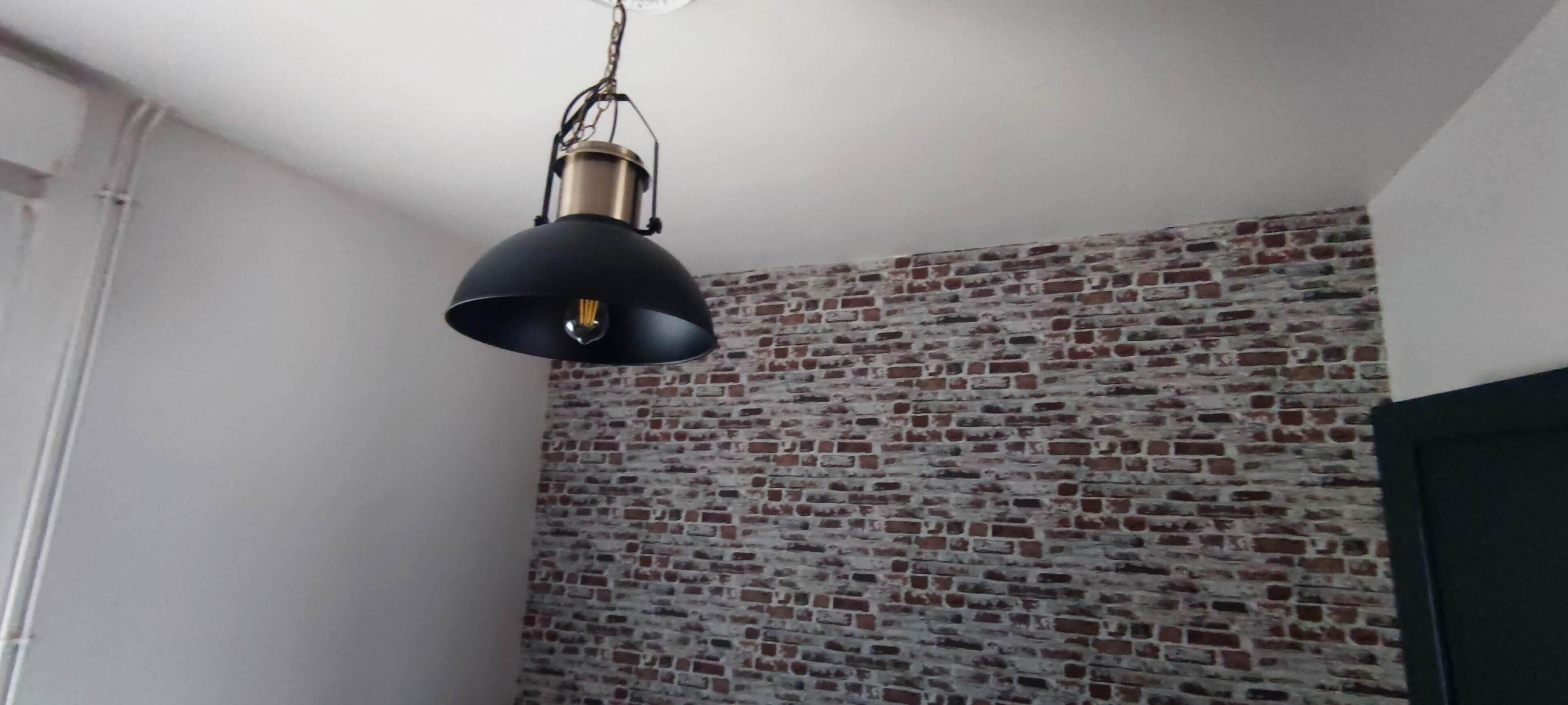 Une pièce avec un mur dont le motif est constitué de briques et une suspension noire.