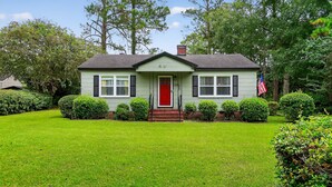 A two-story house with a red front door, a chimney, and a well-maintained lawn. - Cozy Moultrie Home With Backyard Retreat 3 Bedroom Home (Moultrie)