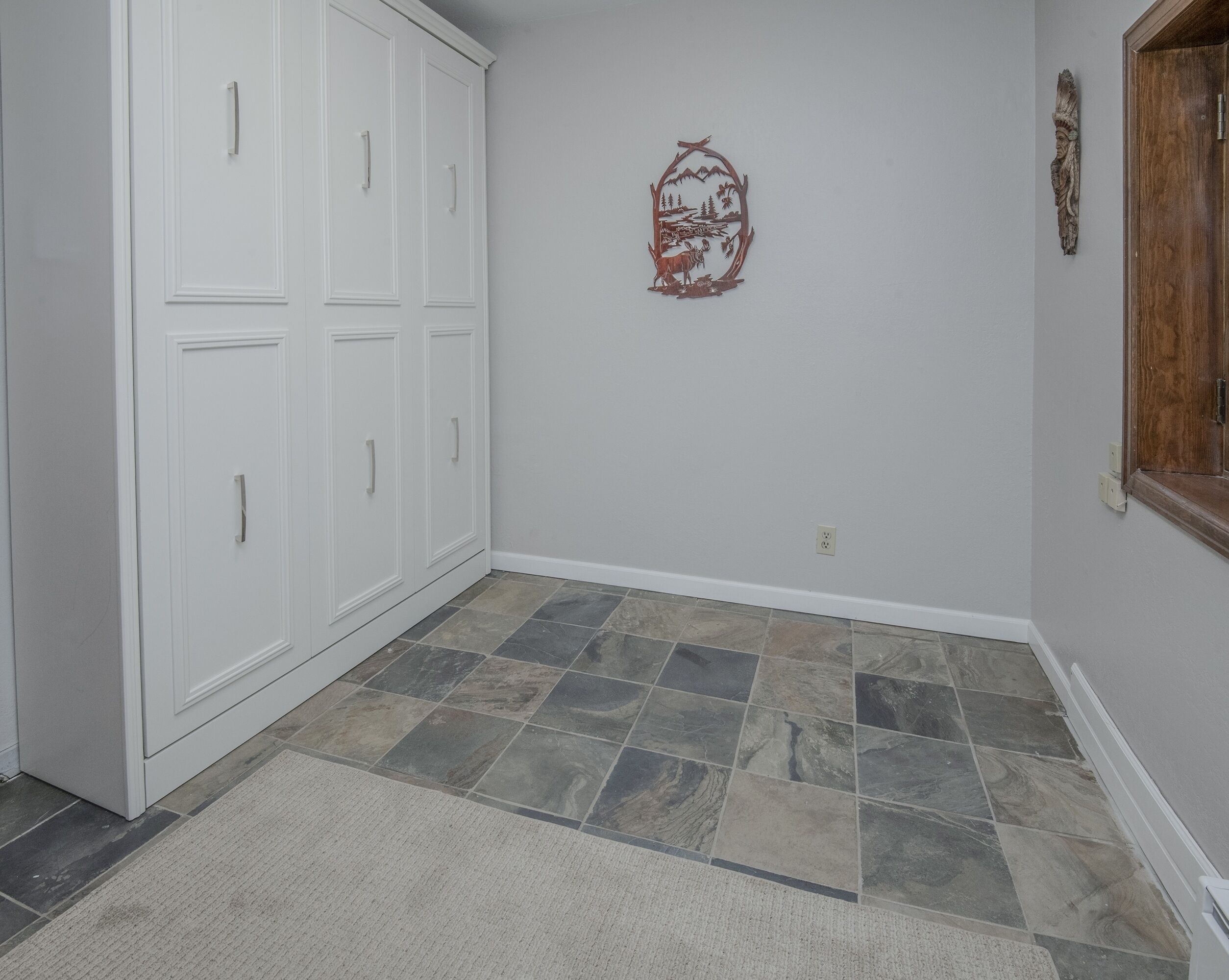 A hallway with a tiled floor, white walls, and a wooden door.