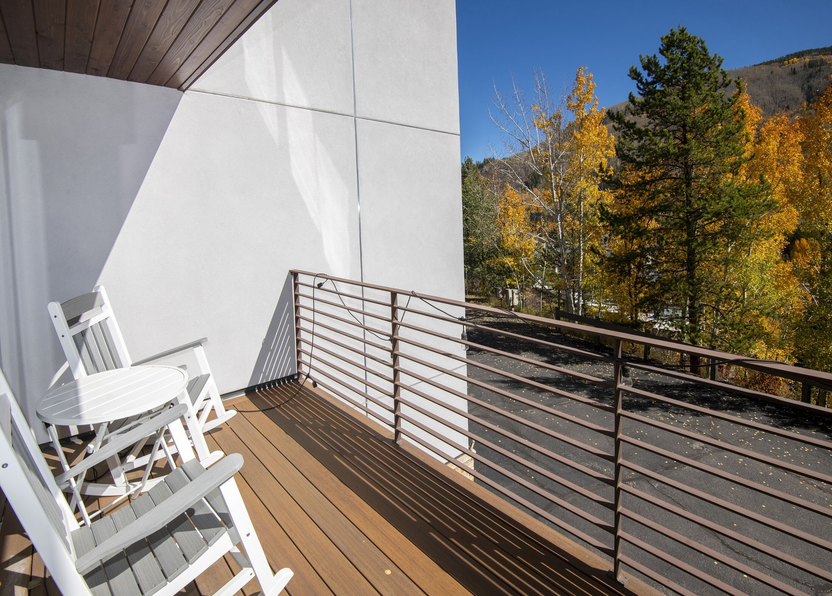 Un balcone con una sedia e un tavolo bianchi, con vista su un'area di parcheggio e alberi autunnali.