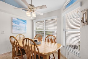 A dining area with a wooden table and chairs, a ceiling fan, and a painting on the wall. - 5550 Palmetto Paradise: 3br W/ Gulf Views, Heated Pool 3 Bedroom Home (Fort Myers Beach)