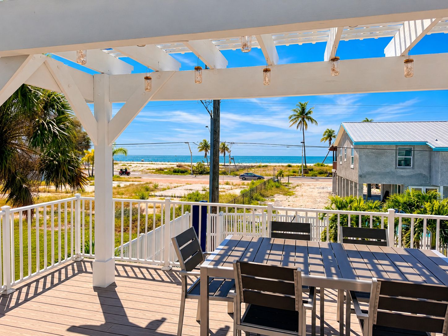 Une terrasse extérieure couverte avec vue sur la plage, une table avec des chaises et une rambarde blanche.