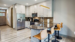 A modern kitchen with a central island, stainless steel appliances, and bar stools. - 1820 The Seasons 1 Bedroom Condo (Keystone)